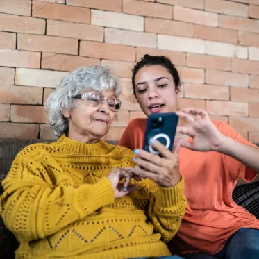 An older woman looking at her phone and a younger woman explaining something, pointing at the screen.