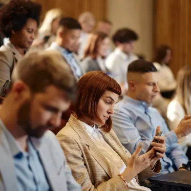 Crowd seated in an auditorium, looking at their phones.