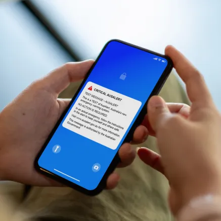 Photo of hands holding a phone with the AusAlert test message on the screen.