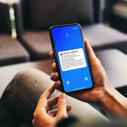 Photo of hands holding a phone with the AusAlert test message on the screen.