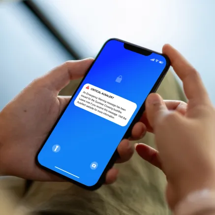 Photo of hands holding a phone with a Critical AusAlert on screen.
